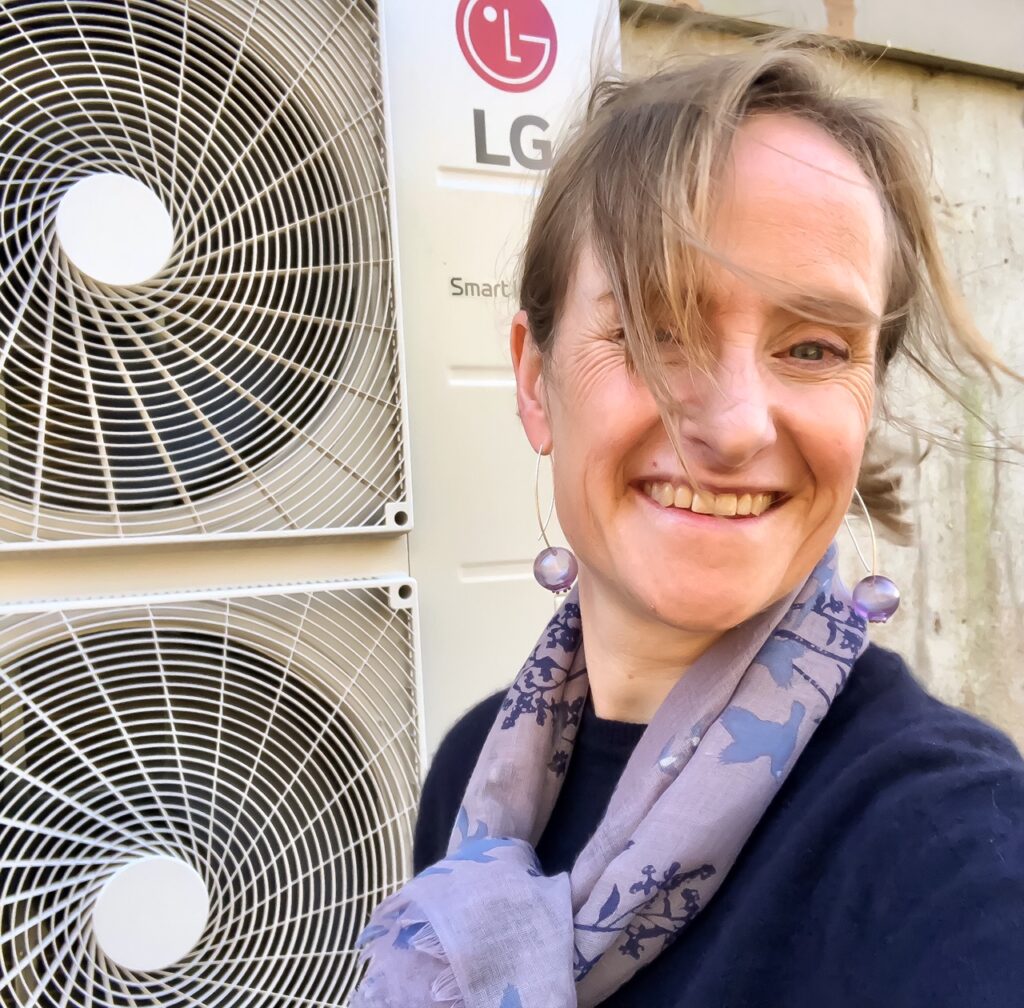 Maurya with a big smile in front of her heat pump.