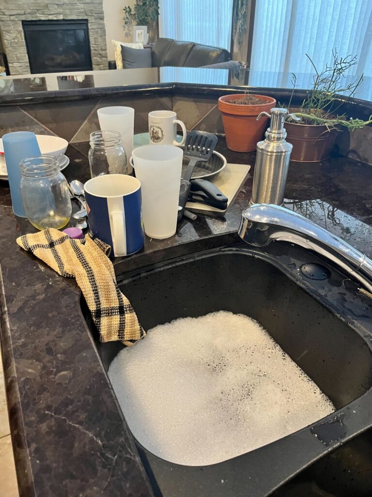 Soapy dish water in a sink with a pile of dishes beside it.